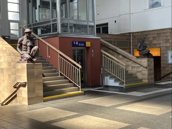 Bahnhofshalle, Zwickau, Hauptbahnhof: links und rechts Treppenaufgang zur ehemaligen Mitropa, bewacht von zwei Bergarbeitern, in der Mitte der Fahrstuhl
