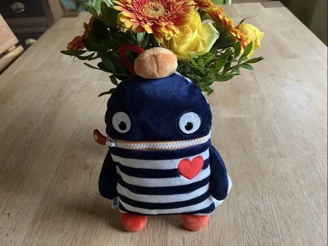 Sorgenfresser aus Velours, blau-weiß gestreift mit orangefarbenen Füßchen vor einem Blumenstrauß zum Schulanfang