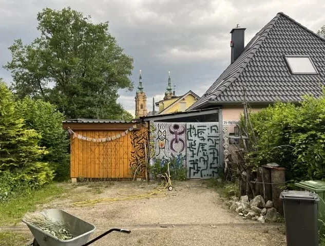 Basilika Vierzehnheiligen im Hintergrund, davor ein bunt benaltes Hoftor, im Vordergrund eine Schubkarre