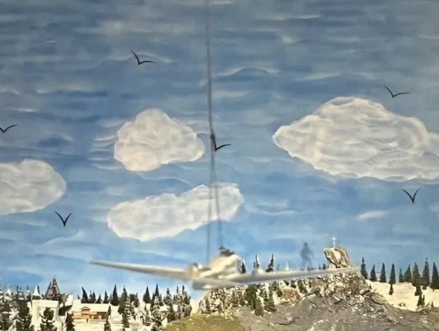 Flugzeug mit Artist auf der rechten Tragfläche vor blauem Himmel mit weißen Wölkchen als Teil einer Modellbahnanlage
