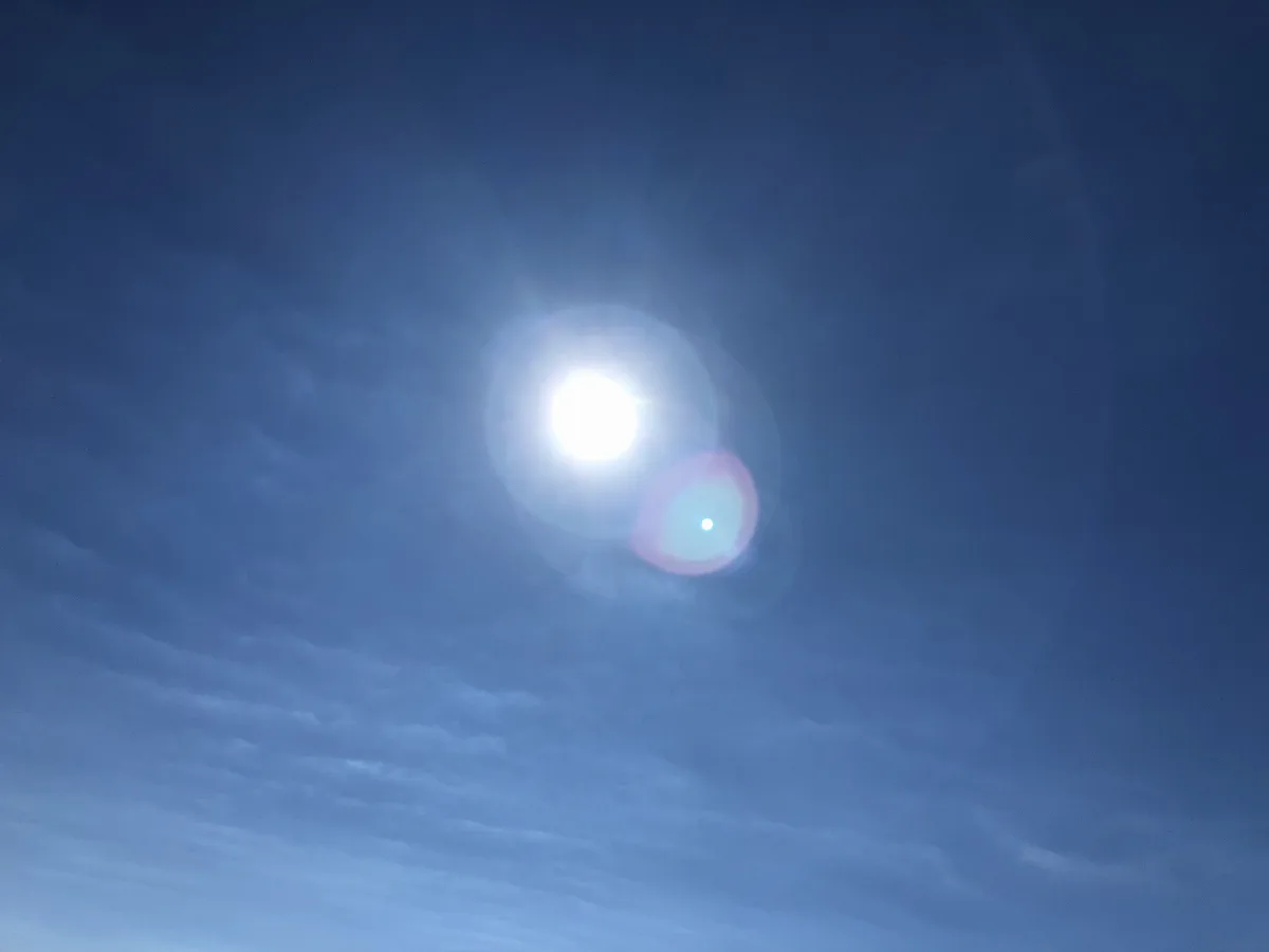 Blauer Himmel mit strahlender Sonne und einem kleinen Reflex-Punkt