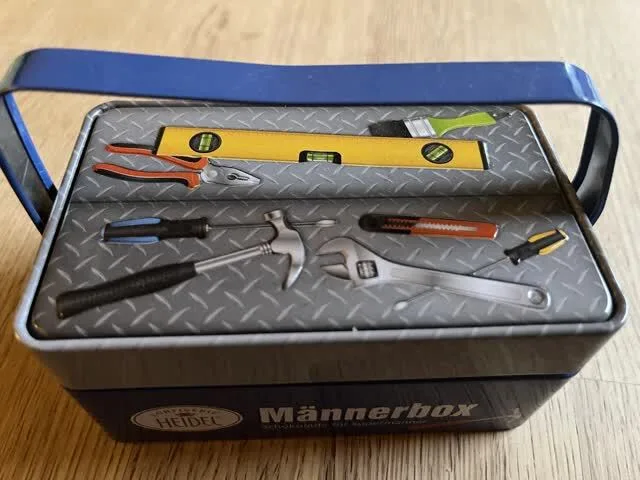 Blechschachtel für Schokolade in Form eines Werkzeugkoffers mit Bildern von Wasserwaage, Hammer, Schraubendreher, Zange…